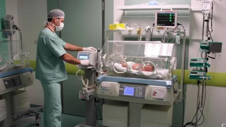 Quanto dura a pós em UTI Neonatal e Pediátrica? Entenda a duração ideal 8 Profissional da enfermagem com especialização em UTI Neonatal regulando ventilador e monitor multiparamétrico ao lado de recém-nascido em incubadora hospitalar.