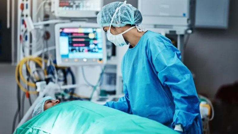 Enfermeiro avaliando paciente em leito de UTI com equipamentos avançados de monitorização.