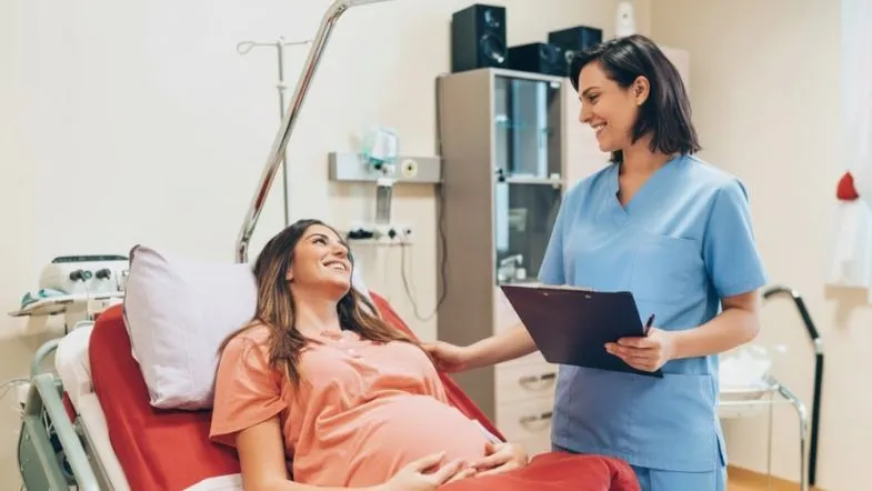 Profissional da Enfermagem Obstétrica conversando e acolhendo gestante em sala de pré-parto.