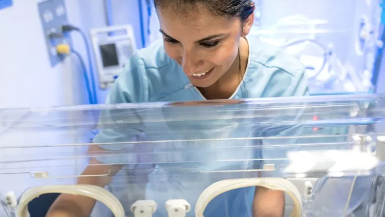 Apgar, reanimação e ventilação: o guia completo da prática em UTI Neonatal e Pediátrica em 2025 9 Profissional de saúde sorrindo enquanto presta cuidados a um recém-nascido dentro de incubadora da UTI.