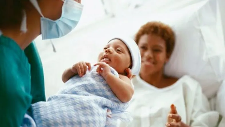 Profissional de enfermagem apresentando o recém-nascido à puérpera no pós-parto imediato.