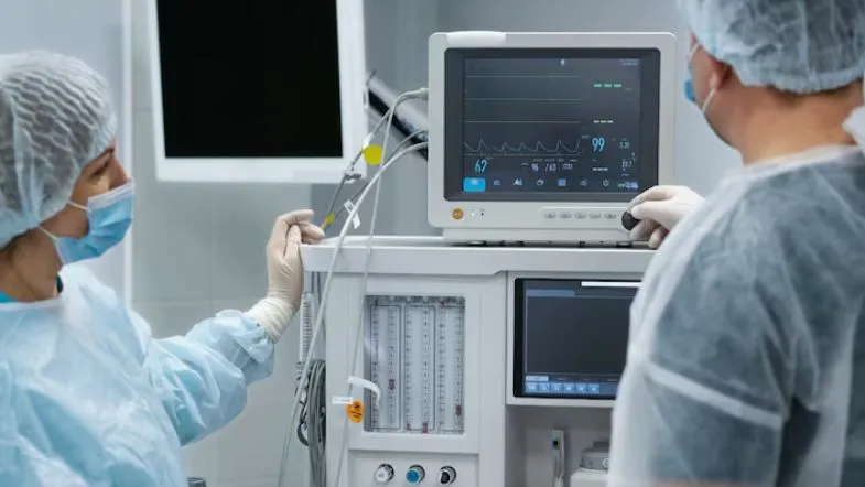 Profissionais da saúde observando monitor multiparamétrico em unidade de emergência, avaliando sinais vitais e parâmetros clínicos.
