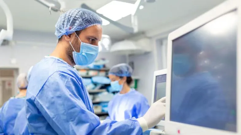 Enfermeiro ajustando monitor hospitalar em ambiente cirúrgico, demonstrando competências essenciais para urgência e emergência.