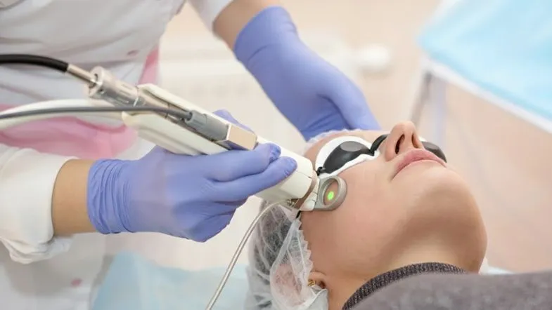 Profissional operando aparelho de laser em tratamento estético facial, representando tecnologias modernas na estética avançada.