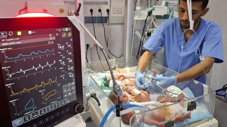 Enfermeiro atua em UTI Neonatal ao lado de incubadora regulando parâmetros ventilatórios de recém-nascido sob cuidados críticos.