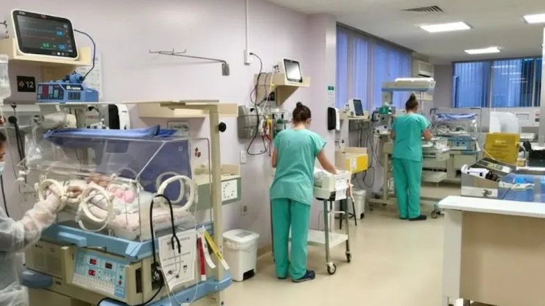 Profissionais de saúde trabalhando em uma UTI Neonatal equipada com incubadoras e monitores de suporte à vida.