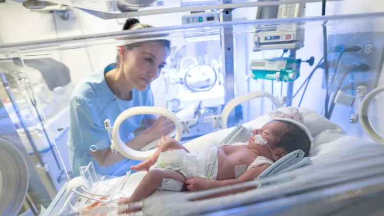 Enfermeira observando e monitorando um bebê prematuro dentro de incubadora na UTI Neonatal.