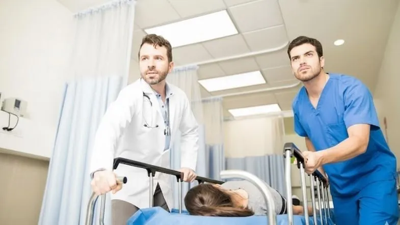 Por que a pós-graduação em Urgência e UTI acelera sua carreira em 2026 6 Profissionais conduzindo paciente em maca em cenário de urgência hospitalar, com foco em atendimento rápido e tomada de decisão clínica.