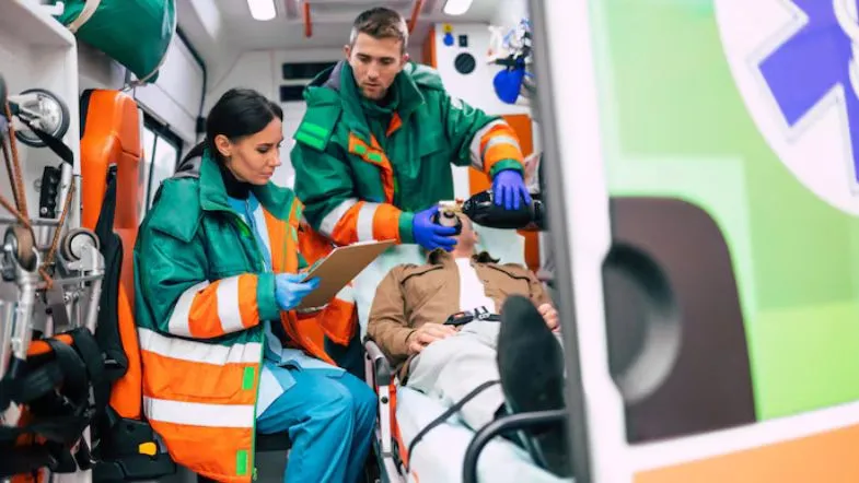 Equipe multiprofissional realizando atendimento de emergência pré-hospitalar com paciente imobilizado em maca.