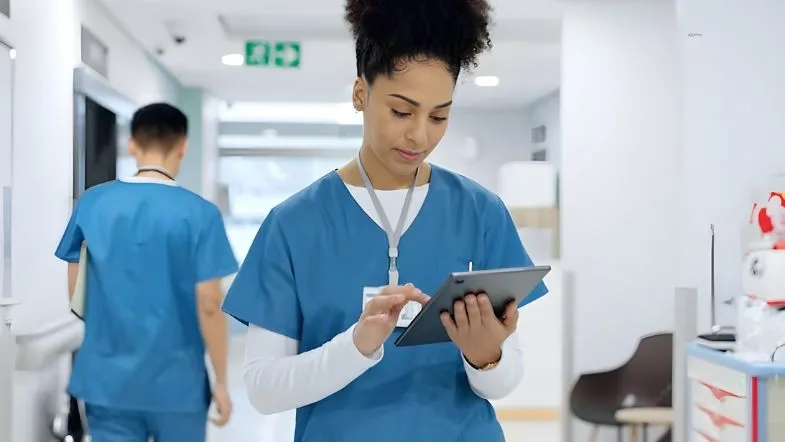 Enfermeira utilizando tablet em corredor hospitalar, demonstrando organização do cuidado e gestão de processos assistenciais.