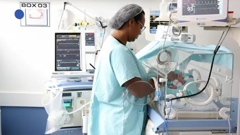 Pós-graduação em UTI Neonatal e Pediátrica: como alavancar sua carreira na saúde em 2026 8 Profissional de saúde de perfil operando monitor multiparamétrico de alta tecnologia acoplado a uma incubadora neonatal.