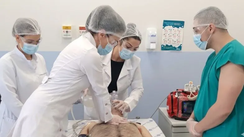 Urgência, Emergência e UTI: como a prática clínica diferencia o enfermeiro especialista 8 Quatro profissionais de saúde em treinamento de simulação realística realizando manobras de ressuscitação cardiopulmonar (RCP) em um manequim.