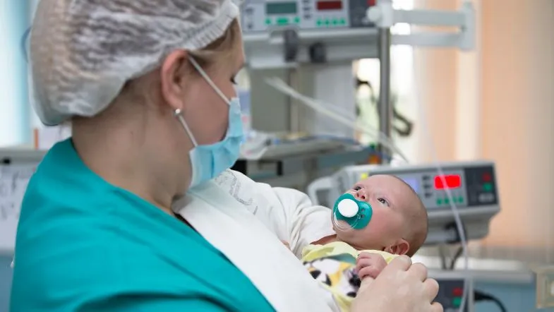 Profissional de saúde oferecendo cuidado humanizado a bebê internado na UTI Pediátrica, com foco em conforto e segurança do paciente.