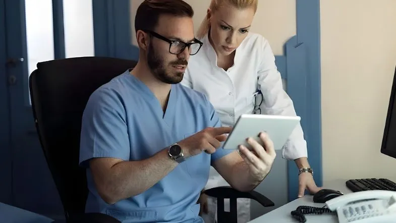 Enfermeiro e médica analisando dados em tablet, representando liderança multiprofissional e gestão colaborativa em saúde.