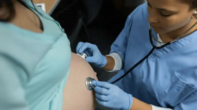 Enfermeira obstetra auscultando batimentos cardíacos fetais em gestante, representando a prática clínica especializada na Enfermagem Obstétrica.