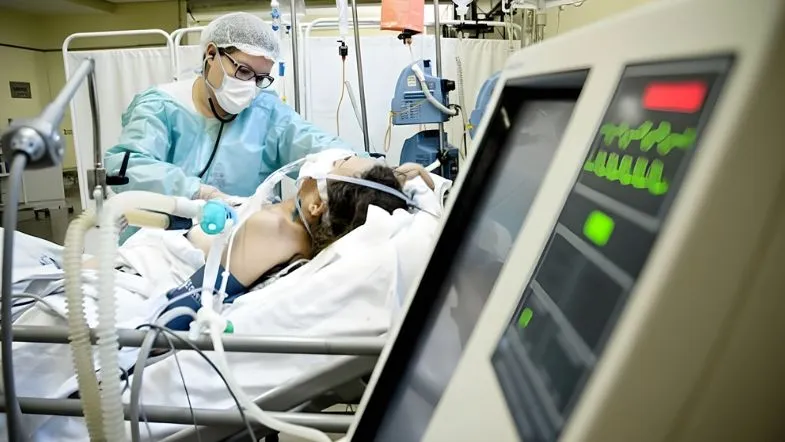 Profissional de saúde prestando assistência ao paciente crítico em UTI com uso de tecnologia e protocolos de enfermagem.