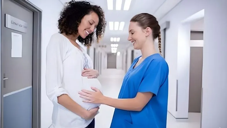 Enfermeira obstetra acompanhando gestante durante consulta em corredor de hospital.